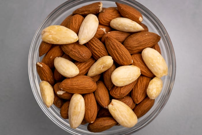 Peeled and unpeeled almonds in a glass bowl